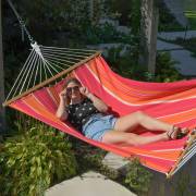 Woman lying in the red and orange spreader bar hammock in a garden