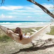 Woman lying in the beige crochet fringe hammock under a tree at the beach