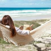 Woman sitting in the beige crochet fringe hammock looking out to the beach