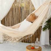 Beige crochet fringe hammock hung in a bamboo cabana with a hat resting on it