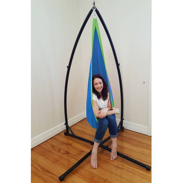 Woman sitting in the blue and green pod chair on the X stand indoors