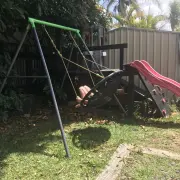 Customer photo of the nest swing in mid swing, with a cubby house and slide behind