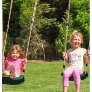 Two girls on green swing seats hung on ropes, with trees behind