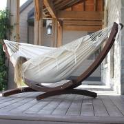 Woman lying in the beige fringe hammock on its wood arc stand on a timber deck