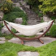 Beige fringe hammock on its wood arc stand in a garden below stone steps