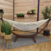 Beige fringe hammock on its wood arc stand on a covered patio with a rug