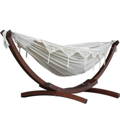 Beige cotton hammock with crochet fringe on a dark wood arc stand, on white
