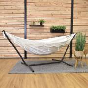 Beige fringe hammock on its steel stand on a covered patio with a rug