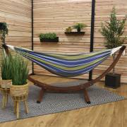Blue and green striped hammock on its wood arc stand on a covered patio with a rug