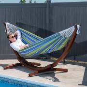 Woman lying in the blue and green striped hammock on its wood arc stand beside a pool