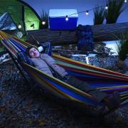 Man lying in the mixed bright colours hammock on its steel stand at a campsite at night