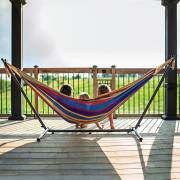 Two children sitting in the mixed bright colours hammock on its steel stand on a deck