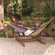 Woman lying in the mixed bright colours hammock on its wood arc stand in a courtyard