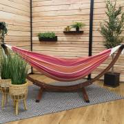 Red and orange hammock on its wood arc stand on a covered patio with a rug