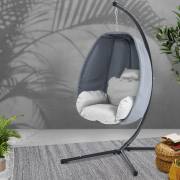 Grey hanging egg chair with cushion and pillow on its curved steel stand, in a room with plants
