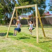 Two girls on the double swing set in a backyard