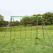 The steel swing set with two green swing seats and a glider on a lawn, with trees behind