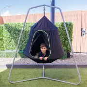 Boy sitting inside the cocoon tent swing hanging from its steel frame on a lawn