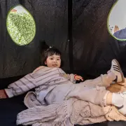 Young girl lying on a blanket inside the cocoon, with the round window behind her