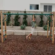 Boy swinging along the monkey bars over bark mulch in a backyard