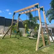 Timber monkey bar and swing set on a lawn beside a house