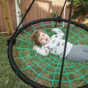 Toddler lying in the green rope web of the swing, seen from above