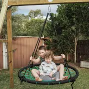 Two young children sitting together in the web swing under the timber frame