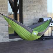 Green and grey parachute hammock hung on a deck beside a stone house