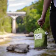 Green parachute hammock packed into its stuff sack, held by a hand at a creek