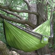 Green and grey parachute hammock hung between the branches of a large tree