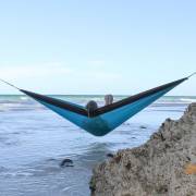 Person lying in the turquoise parachute hammock looking out to sea