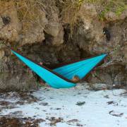 Turquoise parachute hammock hung between rocks on a beach