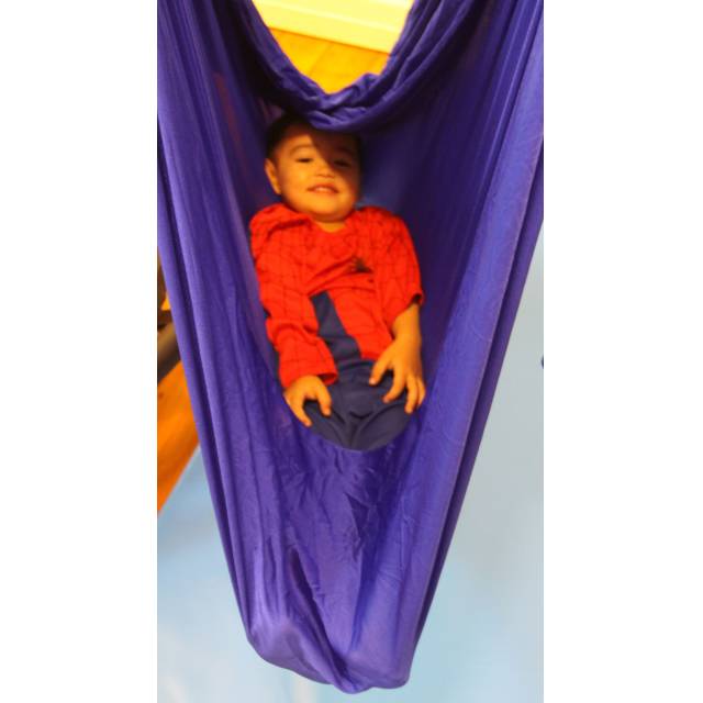 Boy lying inside a blue nylon wrap swing hung from a single point