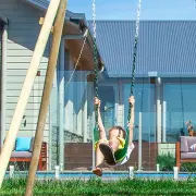 Boy swinging on a green belt swing beside the timber A-frame legs