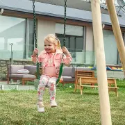 Young girl sitting on a green belt swing beside the timber leg