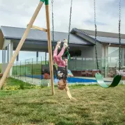 Girl hanging upside down from the trapeze bar beside a green belt swing