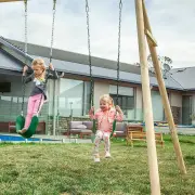 Two girls on the green belt swings beside the timber A-frame legs
