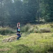 Child holding the trolley handlebar and riding the flying fox across a grassy paddock