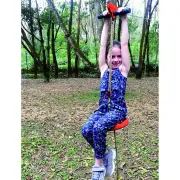 Girl holding the trolley handlebar and sitting on the red disc seat as she rides the flying fox between trees