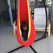 Child sitting in the red and yellow pod chair on the X stand indoors