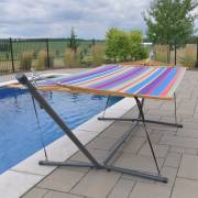 Multi colour spreader bar hammock hung on chains from the 3.7m stand beside a pool, with ropes tying the hammock down to the eyelets on the feet