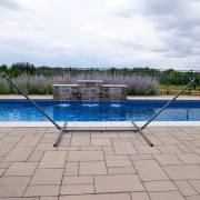 Charcoal steel spreader bar hammock stand beside a pool, seen from the end