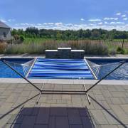 Blue striped spreader bar hammock on the three beam stand beside a pool, seen from the end