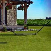 Three beam steel hammock stand on a lawn beside a stone house
